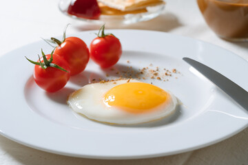 Fried egg with tomatoes on white plate, breakfast dining table