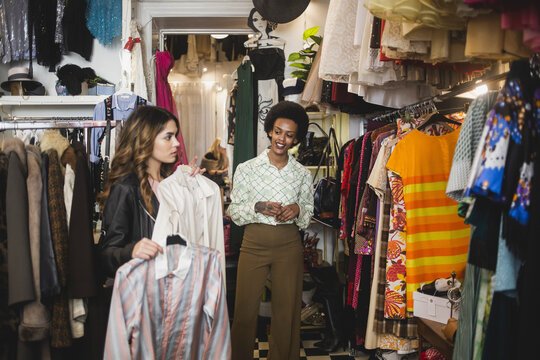 Ung kvinna tittar på kläder medan butiksägare står bredvid