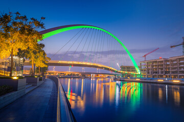 Illuminated in green color Tolerance Bridge in Dubai with an unusual architectural design against the backdrop of skyscrapers. Urbanism and sightseeing in the UAE
