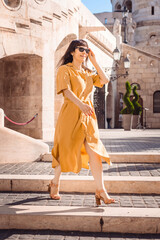 Solo traveler woman portrait. Stylish fashionable happy mature woman traveler wearing yellow dress walks in the center of a european city. People travel regeneratively these days by bike, train, foot.