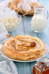  Homemade thin pancakes with honey stacked in a stack, on a wooden table with a mug of milk, a pot of sour cream and eggs in a basket. Traditional Slavonian, pagan holiday (Maslinitsa). Country style 