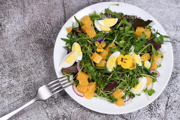  Spring fruit, citrus and vegetable salad from a mix of lettuce leaves and sprouts of radish and lentils, arugula, microgreens, quail egg wedges, with edible flowers - pansies