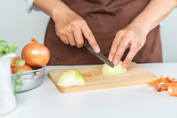 Woman cutting fresh onion on wooden board in kitchen. prepare to cook.