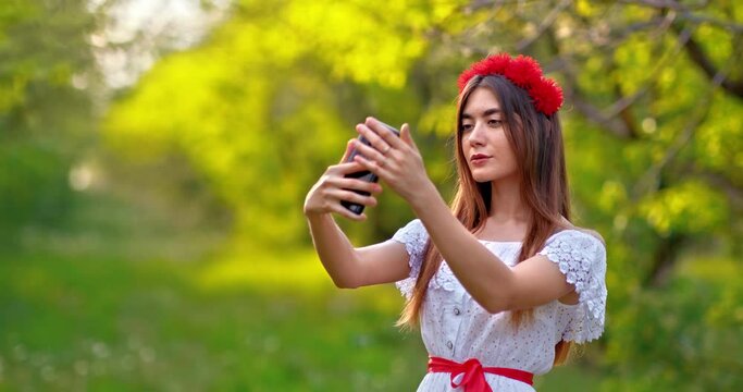 Portrait of a beautiful girl of oriental appearance makes a selfie photo on a mobile phone. Girl looks at the camera and smiles, posing. Zoom in the camera. 4k, ProRes