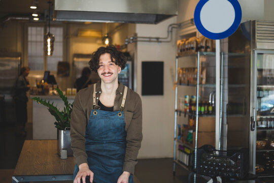 Portr&auml;tt av leende man med f&ouml;rkl&auml;de sitter p&aring; bord i butik