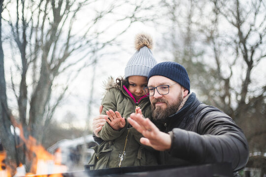 Pappa med dotter v&auml;rmer h&auml;nder vid brasa utomhus