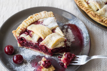 One piece of cherry pie cake with a fork on grey plate on light linen textile background, selective focus