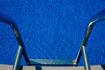Steps to the pool, blue clear water in the outdoor swimming pool, safe descent to the pool, close-up steps through the water