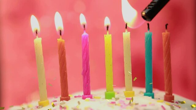 Animation of gold confetti falling over colourful birthday cake candles being lit on cake