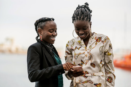 Pleasant black girl friends browsing smartphone