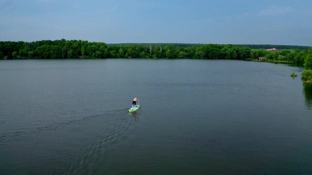 Active adventure on water. Sportsman training on water while standing on a board with oars on the background of beautiful summer landscape. Extreme sport.