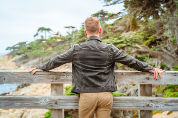 A young man walks in the park near a lonely cypress tree and admires the ocean in California