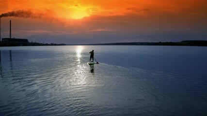 Man sailing on river. Sports training on water against beautiful sunset. Athlete is rowing on the evening water while standing with an oar. Water sports.