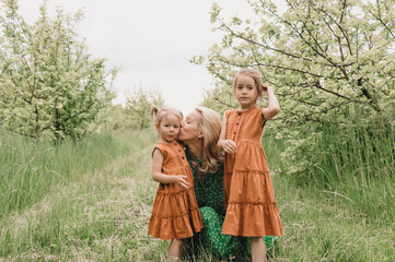 a happy mother hugs and kisses little girls in a green spring garden.