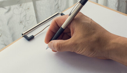 Hand holding a pen on a clipboard. Hand writing on a white paper. 