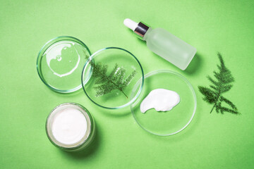 Cosmetic laboratory concept . Glass petri dish with cosmetic products and serum bottles with green plants. Flat lay image.