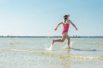 Happy little child girl running and having fun on beach at sunny summer day