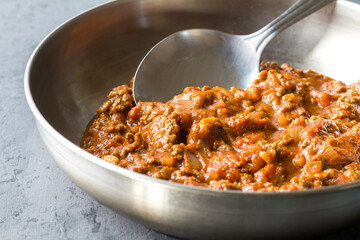 Bolognese (also know as Bolognesa or Bolonhesa) sauce in a pan with ladle on grey background with copy space - studio photo close up