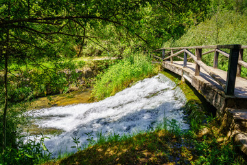 Fototapeta na wymiar Small waterfall under a wooden bridge at the source of the Ebro river. Fontibre Cantabria.