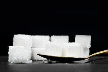 Several white sugar cubes were placed in a brass spoon on a black stone background.