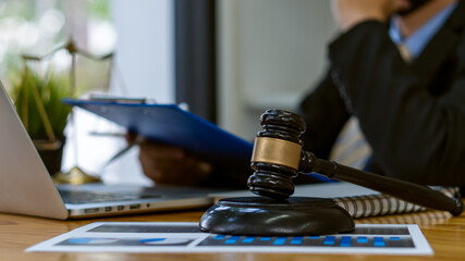 A lawyer or judge works in the office handing the paperwork with a hammer and scales of justice on closeup table