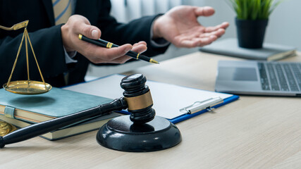 A lawyer or judge works in the office handing the paperwork with a hammer and scales of justice on closeup table