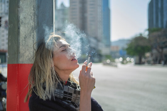 Woman smoking cigarette near city road in sunlight