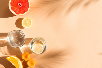 minimalist flat lay with water glass and seasonal fruits. beige summer background with palm tree...
