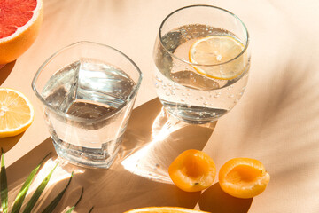 water glasses  with fruit on sunlight close up, fresh and healthy summer drinks beige color background 