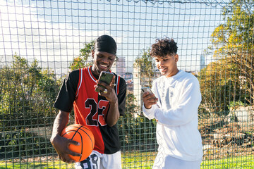 Smiling black men using smartphones on basketball court in city