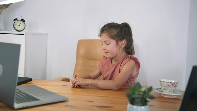 The girl looks at her laptop. The child communicates online while sitting at the table. The child learns online. Home education. The light of a table lamp. Online training Self-isolation Slow motion
