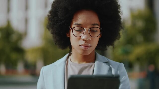 Close up portrait african american young woman hold tablet computer stand on street look at camera . Pretty, suit, career, businesswoman, houses, model, lady, adult, successful. Close up. Slow motion