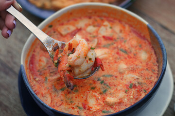 Close up boiled shrimp in the spoon with Tom Yum Kung (Thai Style spicy soup) in the background.
