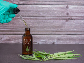 Glass brown bottle with herbal organic cannabis oil (CBD Oil) with label and marijuana leaves on a dark gray with wooden wall background. Space for text. Cannabis for medical and business concept