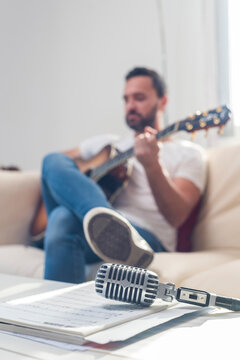 Anonymous man playing guitar on couch near table with retro mic