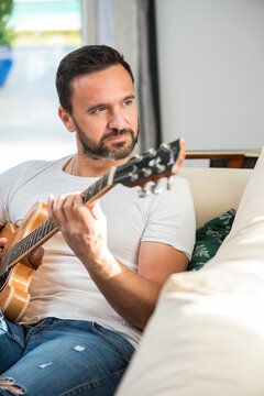 Positive ethnic man playing guitar on couch