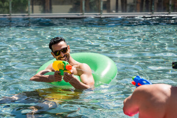 excited muslim man enjoying water pistols battle with friend in swimming pool
