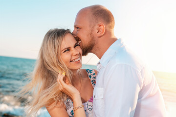 Fototapeta premium A couple of happy young men and women hug and kiss. In the background, the ocean and the sky. Vacation romance concept