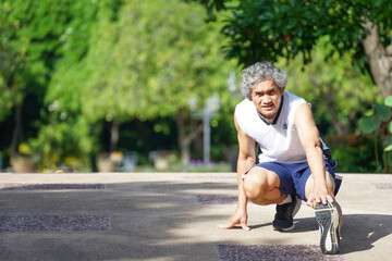 elderly man smiling, runner warming up exercise by stretching his legs in the park at good atmosphere in the morning sunshine,concept aging society,good health, quality of life.