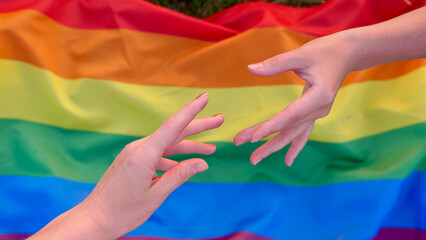 Parody of the mural Creation of Adam on the background of the LGBT flag during the celebration of the month of dignity, Bisexuality Day or National Coming Out Day. Female hands of lesbians
