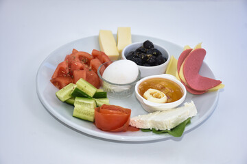 Close up of breakfast foods  with olives, tomatoes, salami, egg, jam, honey, cream, cucumber. Isolated on white.