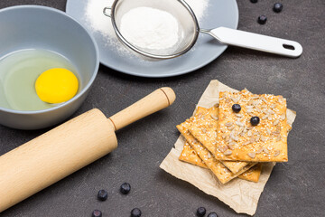 Biscuits sprinkled with seeds and rolling pin on table.