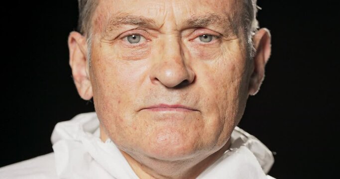 Close-up of an older man's face, with gray hair, wrinkles due to age, mature face, skin, complexion, guy wearing a white apron on a black background, beautiful blue eyes