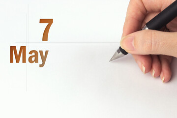 May 7th. Day 7 of month, Calendar date. The hand holds a black pen and writes the calendar date....