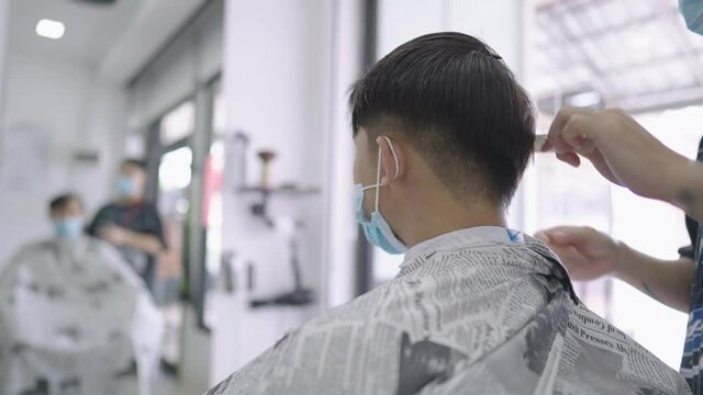 Asian man wear protective face mask get hair cut during quarantine pandemic, electric hair clipper blade, male barber reopening business again, guy hair designer creation, customer service job