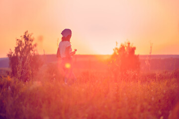 Woman at sunset in a field of wild flowers, headscarf and jeans pants. Beautiful woman feeling relax At the outdoor lawn on a natural blurred background concept Emotional with nature