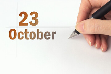 October 23rd. Day 23 of month, Calendar date. The hand holds a black pen and writes the calendar...