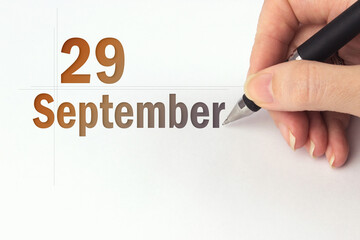 September 29th. Day 29 of month, Calendar date. The hand holds a black pen and writes the calendar...
