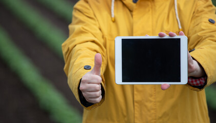 Farmer showing tablet and thumb up in field
