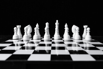 Series of white chess pieces before game on black-white board on black background.